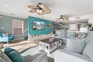A living room with a large TV, ceiling fans, and a dining area with a table and chairs.