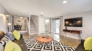 A modern living room with a sofa, a patterned rug, a coffee table, and a TV mounted on the wall.