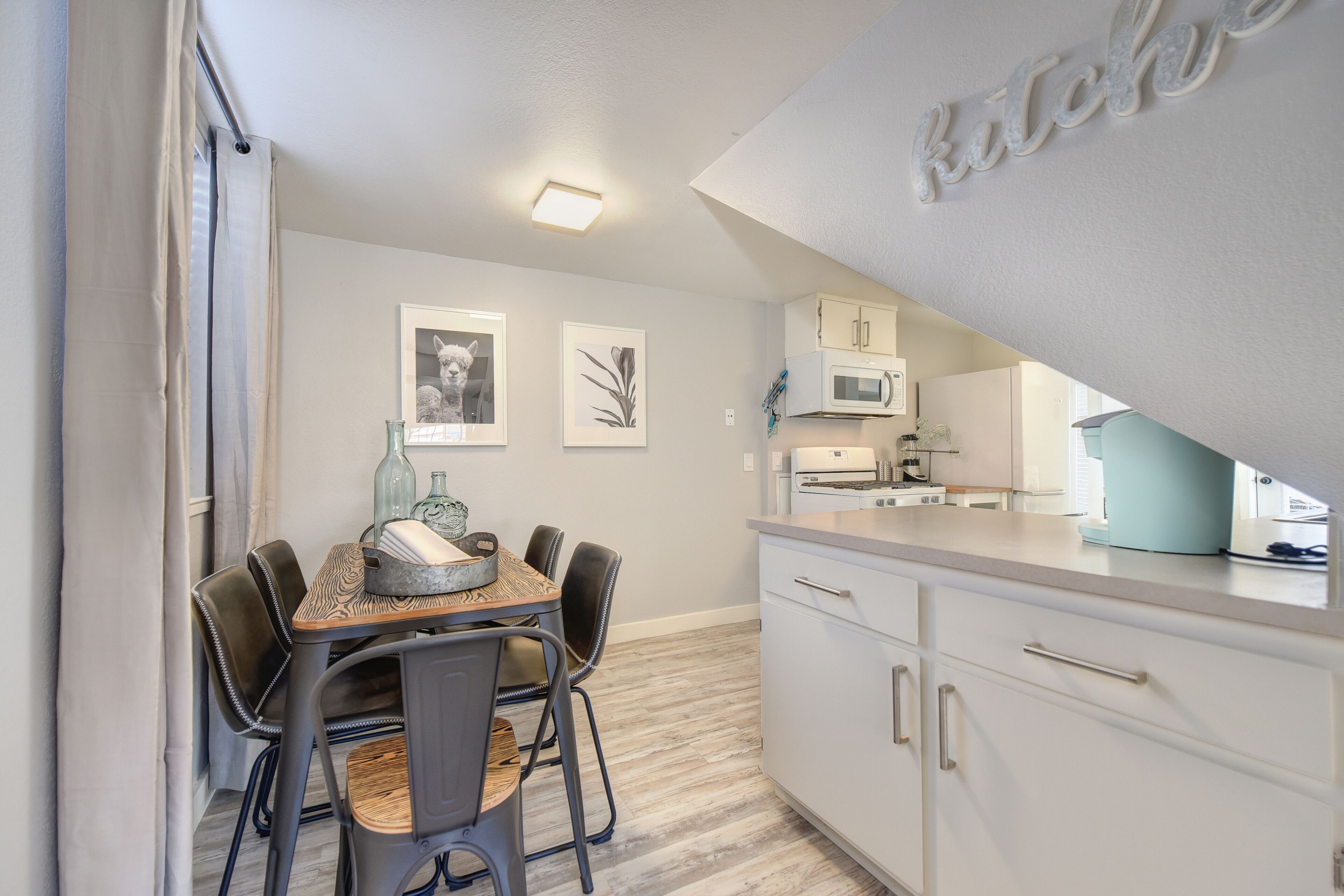 A modern kitchen with white cabinets, a dining table with chairs, and a microwave.