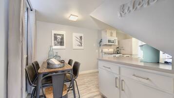 A modern kitchen with white cabinets, a dining table with chairs, and a microwave.