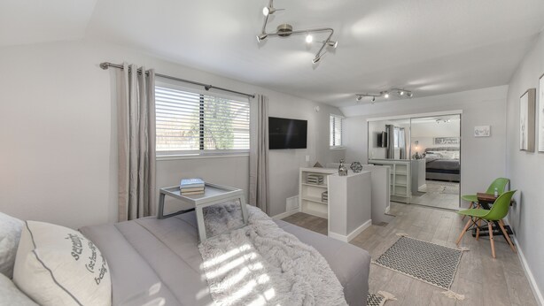 Un dormitorio moderno con cama, mesita de noche y un ventanal con cortinas. En la esquina, hay un escritorio pequeño con una silla y un espejo.