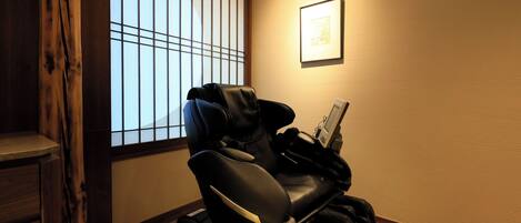 A massage chair in a room with a tatami mat floor, a window with wooden slats, and a framed picture on the wall.