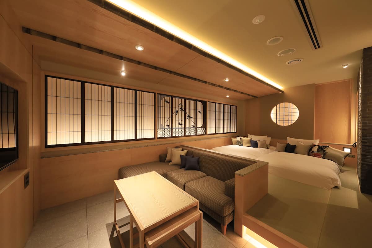 A modern hotel room with a sofa, a small table, a bed, and a traditional Japanese shoji screen.