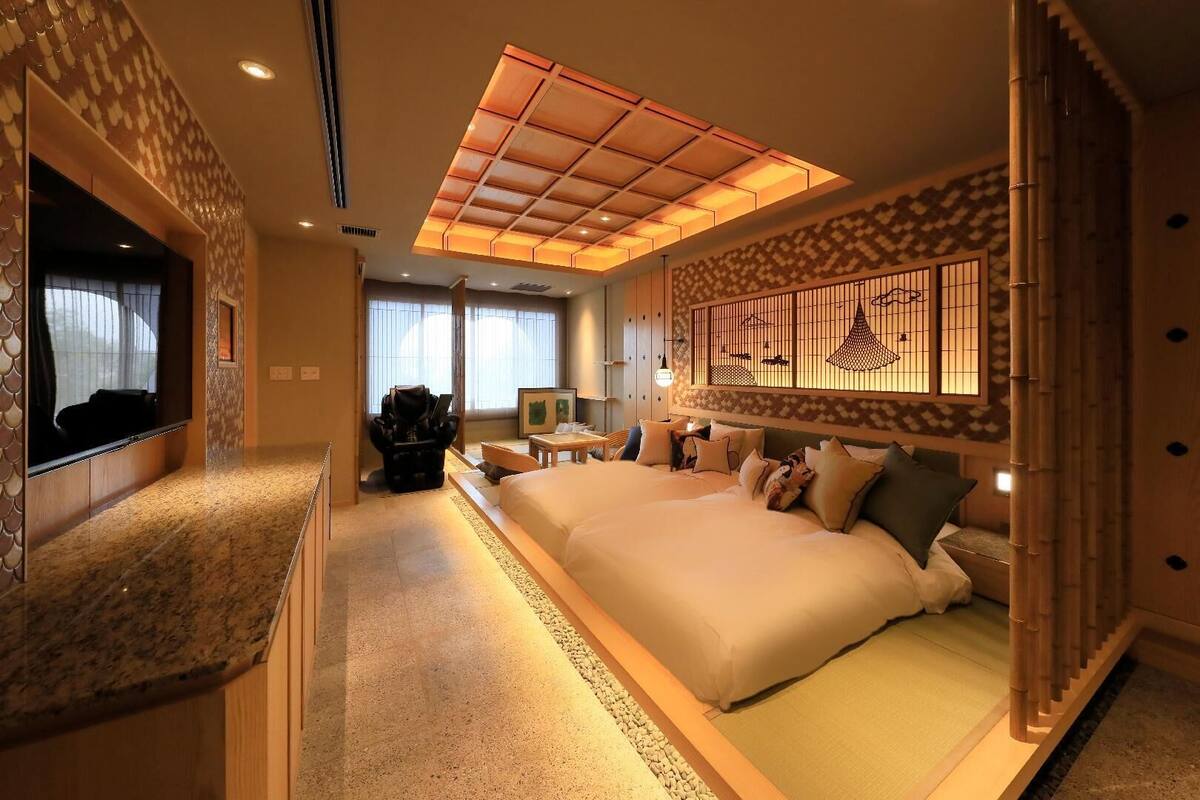 A hotel room with a large bed, a TV, a desk, and a view of the outside.