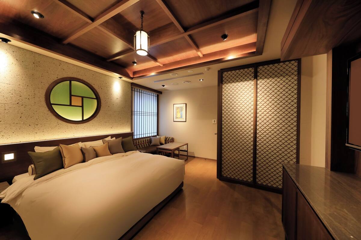 A modern hotel room with a large bed, a small table, and a sliding door.