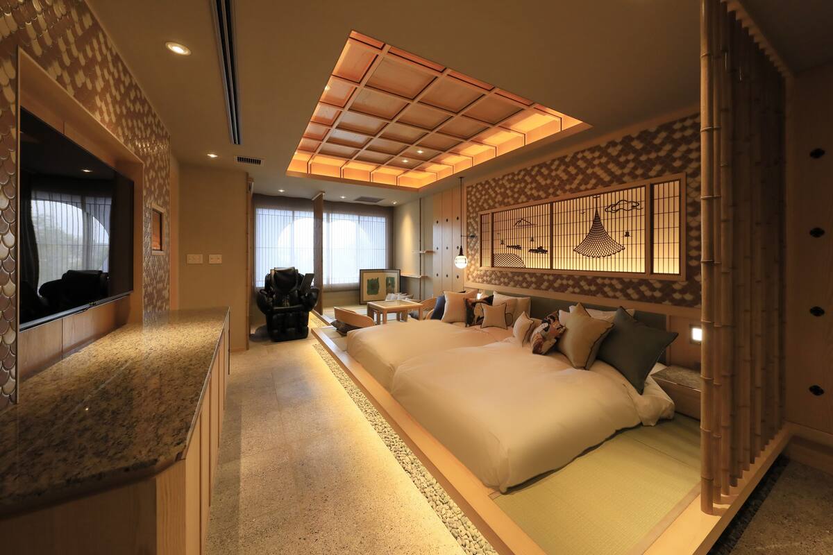 A spacious bedroom with a large bed, a TV, a desk, and a decorative wall.