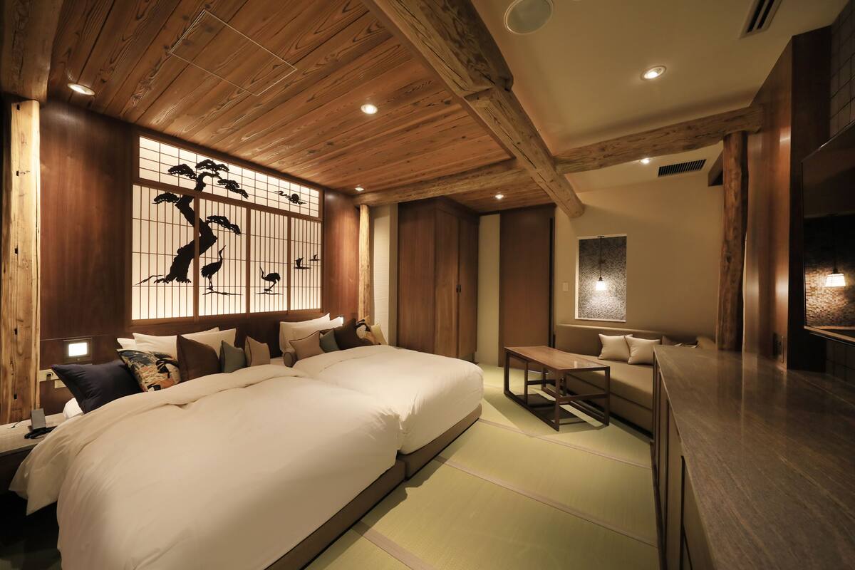 A traditional Japanese-style bedroom with a large bed, wooden ceiling beams, and a shoji screen with artwork.