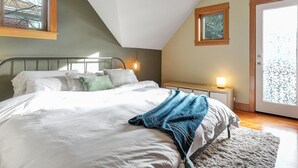 Ein Schlafzimmer mit einem Bett, einem Nachttisch, einer Lampe und Blick ins Freie durch eine Tür.