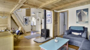 Un salon chaleureux avec un plafond en bois, un poêle en fonte noir, un canapé bleu et une table à manger.