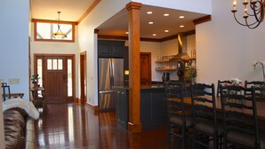 A spacious living area with a wooden floor, a dining table with chairs, a kitchen with a refrigerator, and a chandelier. -  Family  Friendly Retreat on Lake Burton- Sleeps 12 (Clarkesville)