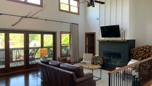 A spacious living room with a fireplace, a large TV, and a balcony with outdoor furniture. -  Family  Friendly Retreat on Lake Burton- Sleeps 12 (Clarkesville)