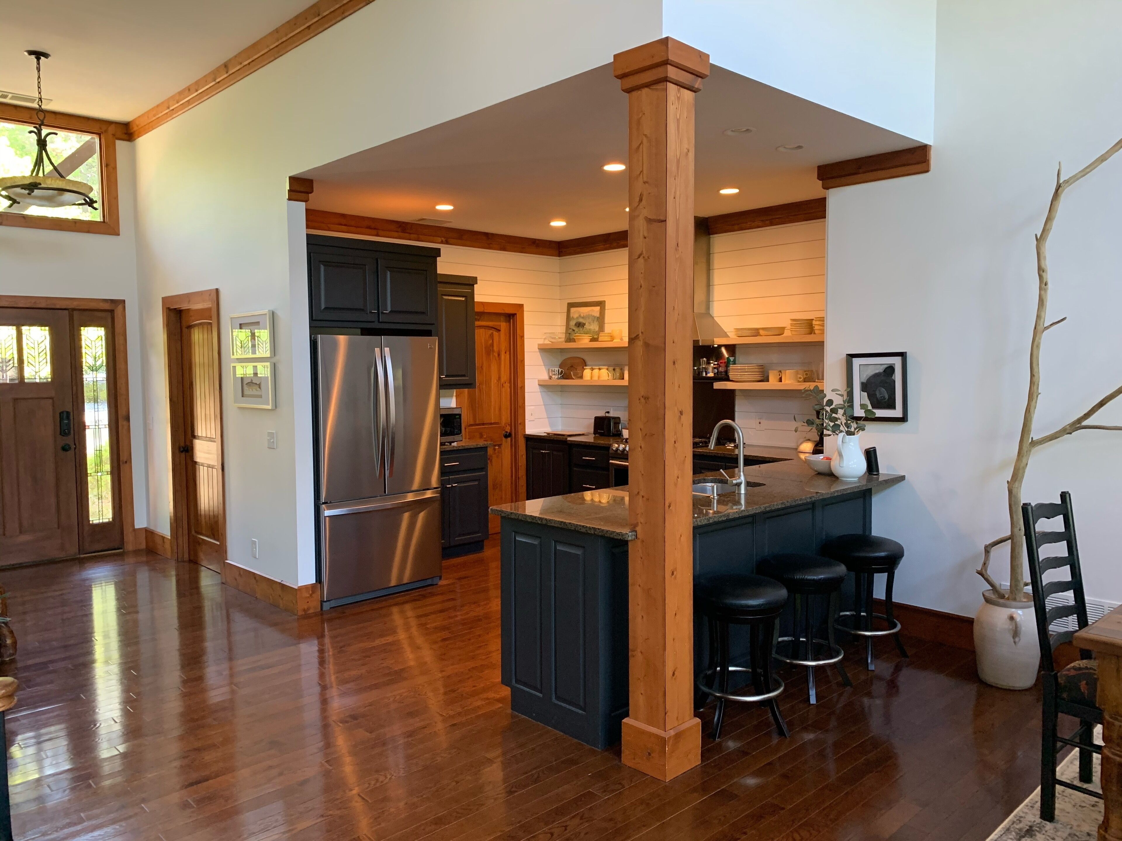 A spacious kitchen with a central island, dark cabinetry, and a stainless steel refrigerator.