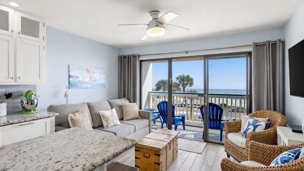 A modern living room with a sofa, chairs, a kitchen area, and a balcony with a view of the sea. - Top Floor! Beachfront View, Two Pools, Walk to Beach (Galveston)