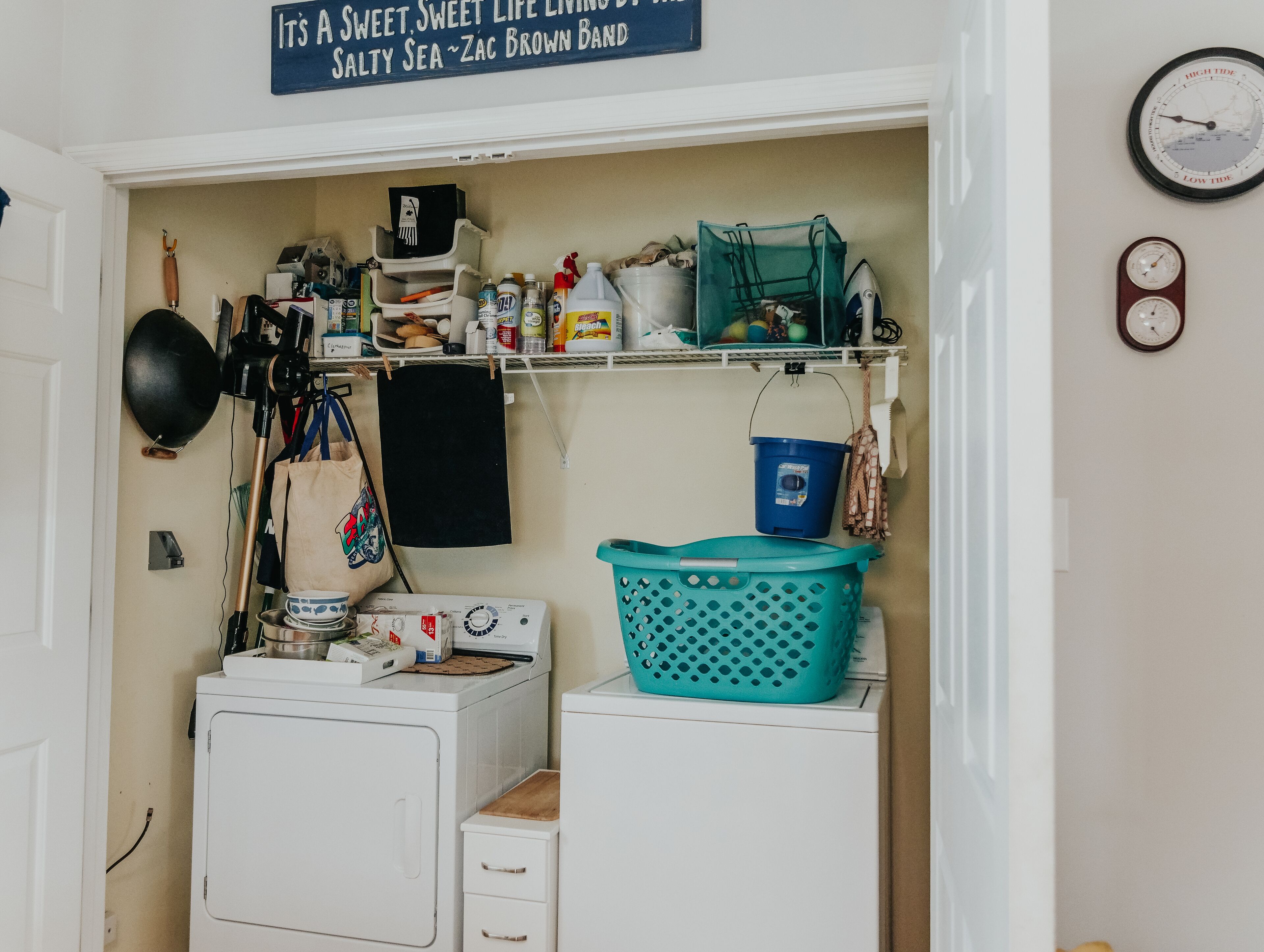A laundry room with a washing machine, dryer, and shelves above containing cleaning supplies and a blue bucket.