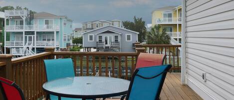 A wooden deck with a round table and colorful chairs, overlooking a row of houses with balconies.