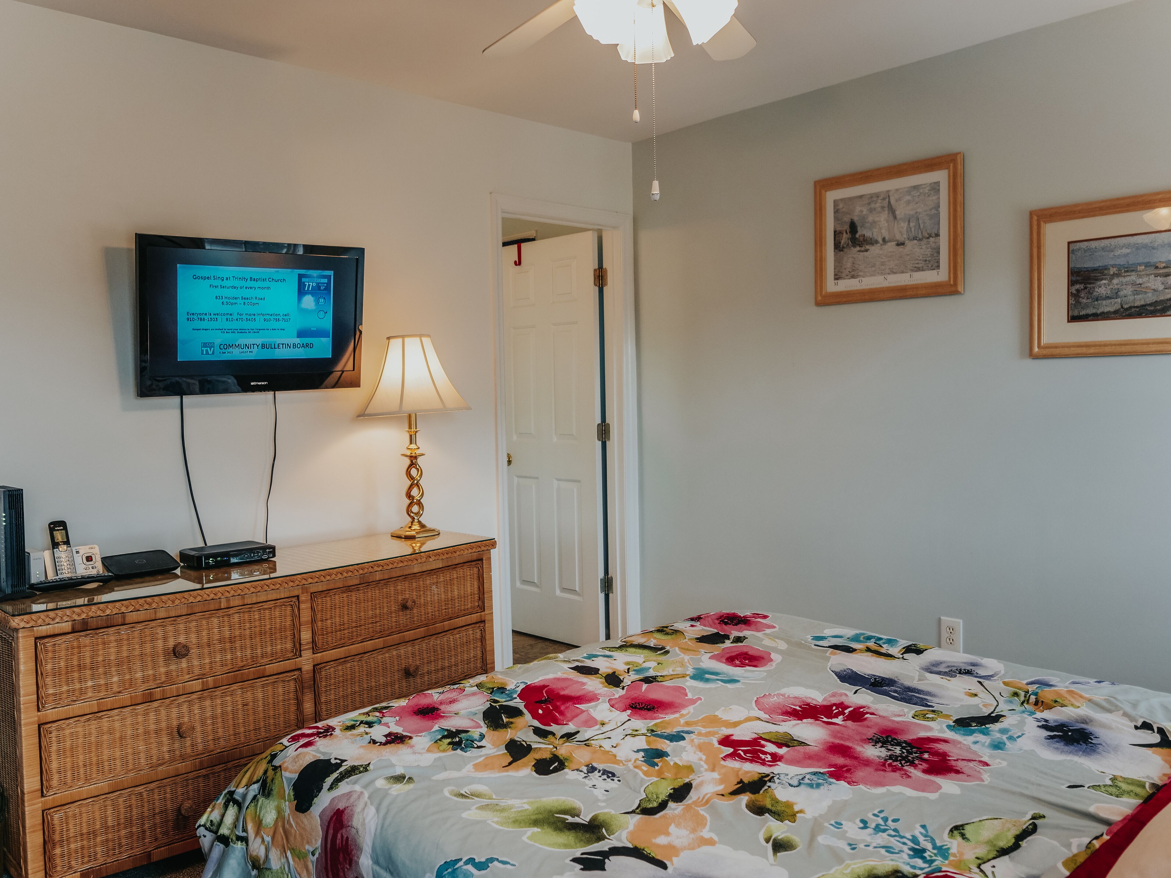 Una habitación con una cama, un aparador, un televisor mostrando un tablón de anuncios y una puerta que da a otra habitación.