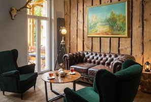 A room with a leather sofa, two green armchairs, a round coffee table, and a painting on the wall. - Bodetaler Basecamp Lodge (Oberharz am Brocken)