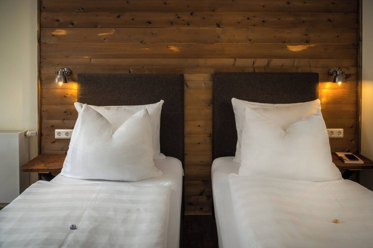Een tweepersoonskamer met twee bedden, houten hoofdborden en bedlampjes.