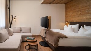 A hotel room with a bed, a sofa, a small table with a book, a TV, and a wall-mounted light. - Bodetaler Basecamp Lodge (Oberharz am Brocken)