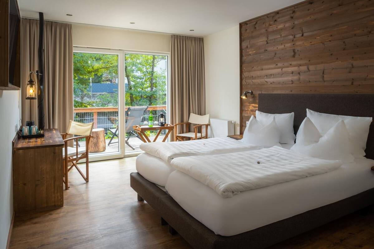 Een slaapkamer met een groot bed, een houten hoofdbord, een bureau met lamp en uitzicht op de omgeving via een schuifdeur.