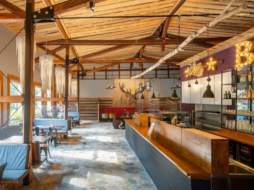 A restaurant interior with a wooden ceiling, stone flooring, and a bar area with a sign that reads 'B&B'.