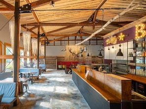 Een restaurantinterieur met een houten plafond, stenen vloer en een bar met een bordje waarop 'B&B' staat.