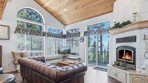 A spacious living room with a leather sofa, a fireplace, and large windows offering a view of the outdoors.