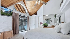 A bedroom with a large bed, a ceiling fan, a sliding glass door to a balcony, and a large painting on the wall.