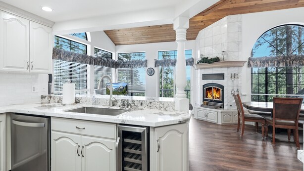 A spacious kitchen with white cabinetry, a built-in dishwasher, a marble countertop, and a fireplace.