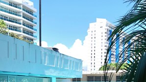 A swimming pool with blue chairs and a white building in the background. - DREAM ESCAPE - TWO BEDROOM OCEANFRONT 
SEAS THE DAY, THE OCEAN IS YOUR NEIGHBOR. (Isla Verde)