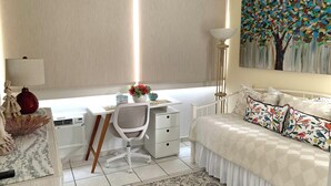 A bedroom with a bed, desk, chair, and a painting on the wall. - DREAM ESCAPE - TWO BEDROOM OCEANFRONT 
SEAS THE DAY, THE OCEAN IS YOUR NEIGHBOR. (Isla Verde)