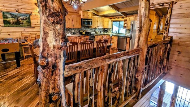 Een landelijk houten interieur met houten wanden en vloeren, een eethoek met een grote houten tafel en stoelen, een keuken met moderne apparatuur en een trap naar een verdieping.