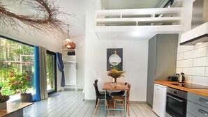 Une cuisine moderne avec des meubles blancs, une table à manger avec des chaises, un petit réfrigérateur et un four encastré.