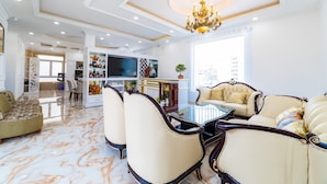 A spacious living room with a glass coffee table, plush seating, a television, and a decorative chandelier. - King Villa (Xuan Huong - Da Lat)