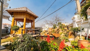 A traditional wooden gazebo with a tiled roof, surrounded by a landscaped garden with a small pond, rocks, and various plants. - King Villa (Xuan Huong - Da Lat)
