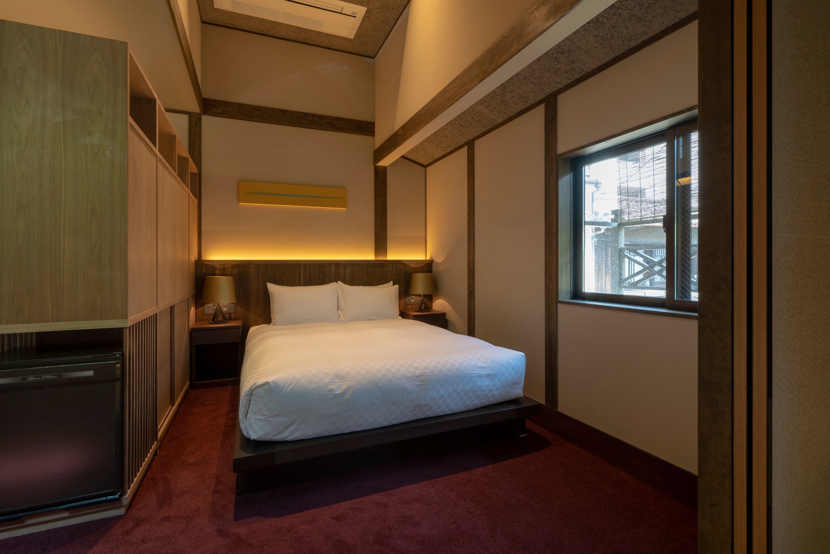 A hotel room with a bed, bedside tables, a window, and a built-in wardrobe.