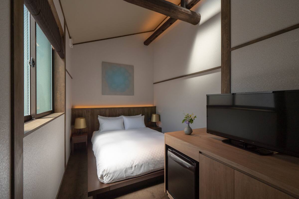 Ein Hotelzimmer mit einem Bett, einem Fernseher, einem kleinen Tisch mit Lampe und einem Bild an der Wand.