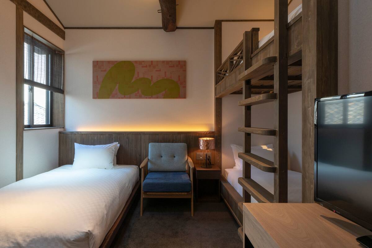Ein Hotelzimmer mit einem Bett, einem Sessel, einem Fernseher, einer Lampe und einem Etagenbett.
