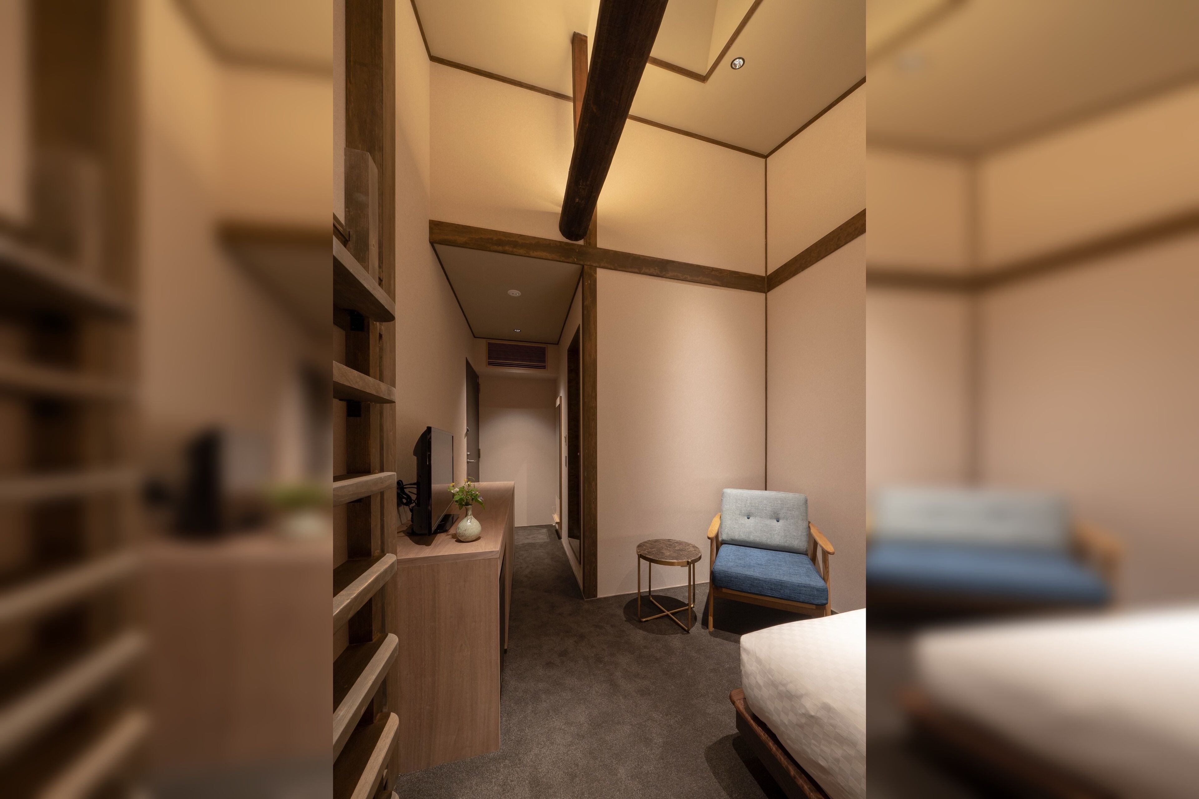 A modern hotel room with a wooden desk, a small round table, a blue armchair, and a bed.