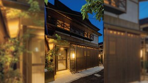 Ein traditionelles japanisches Haus mit Holzfassade, einem sichtbaren Eingang und einem kleinen Garten.