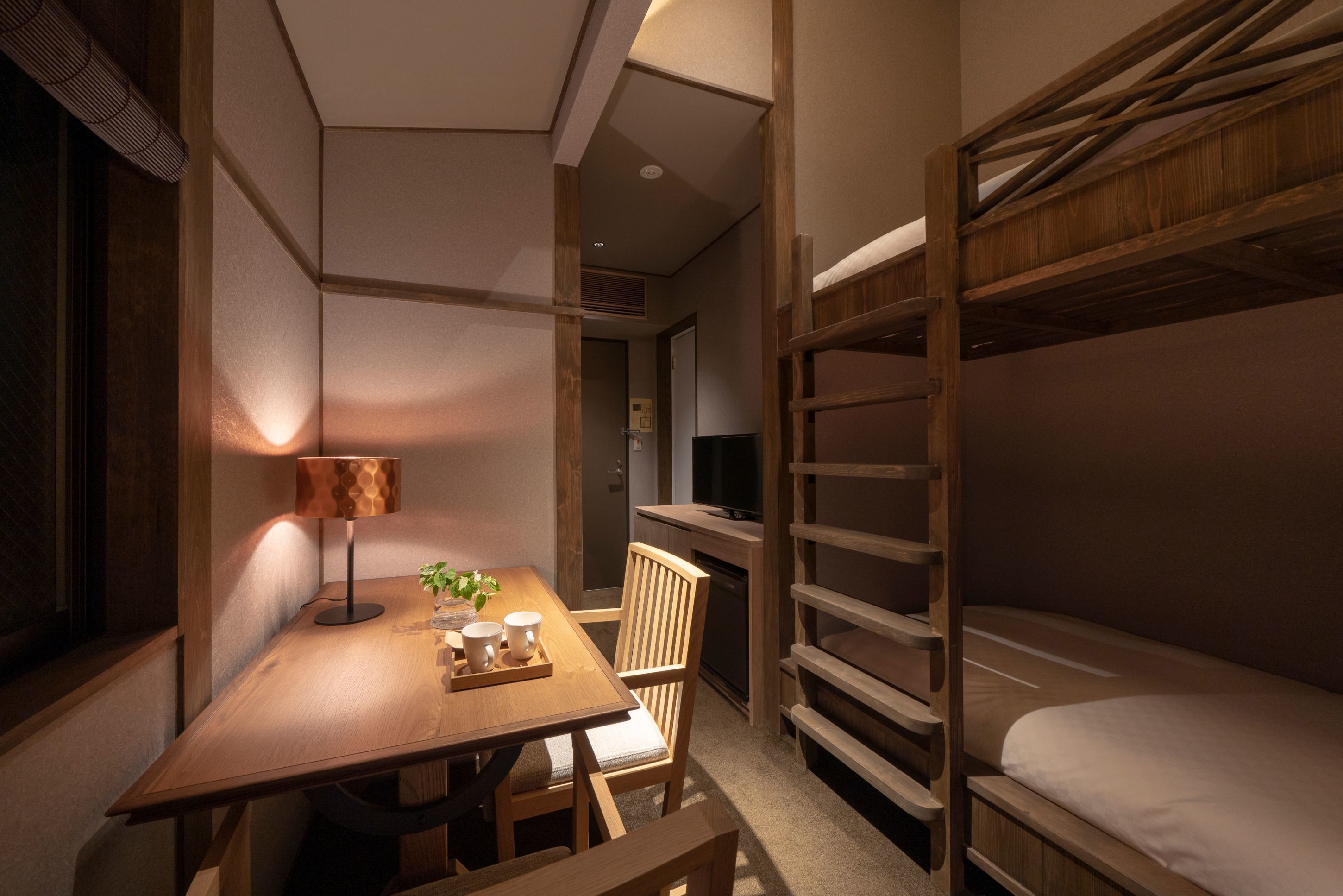Una habitación compacta con literas, una pequeña mesa de comedor con sillas, una lámpara y una kitchenette.