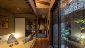 Ein modernes Interieur mit Holzboden, einer Sitzecke mit Kissen, einem kleinen Tisch mit Tassen und einem Teekessel sowie Blick durch ein Fenster mit Jalousien.