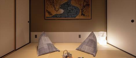Une pièce avec un sol recouvert de tatamis, ornée d’une peinture japonaise traditionnelle, comprenant un service à thé et une petite plante.