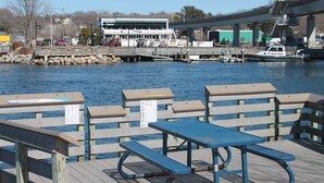 A wooden pier with benches and a table, overlooking a river with boats and a bridge in the background. - Walk to the  beach and Kayak at Black Point, Niantic, Ct. (Niantic)