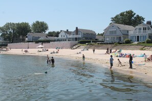 Une plage avec des maisons en arrière-plan et des gens qui profitent de l’eau.