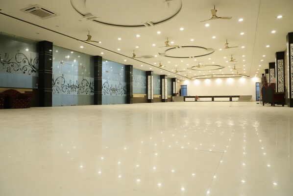 A spacious, well-lit hotel lobby with a polished floor, decorative wall panels, and ceiling fans.
