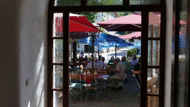 An arched doorway leading to an outdoor seating area with red umbrellas and tables. - Hotel Bayerischer Hof (Burghausen)