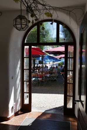 An arched doorway leading to an outdoor seating area with red umbrellas and tables. - Hotel Bayerischer Hof (Burghausen)