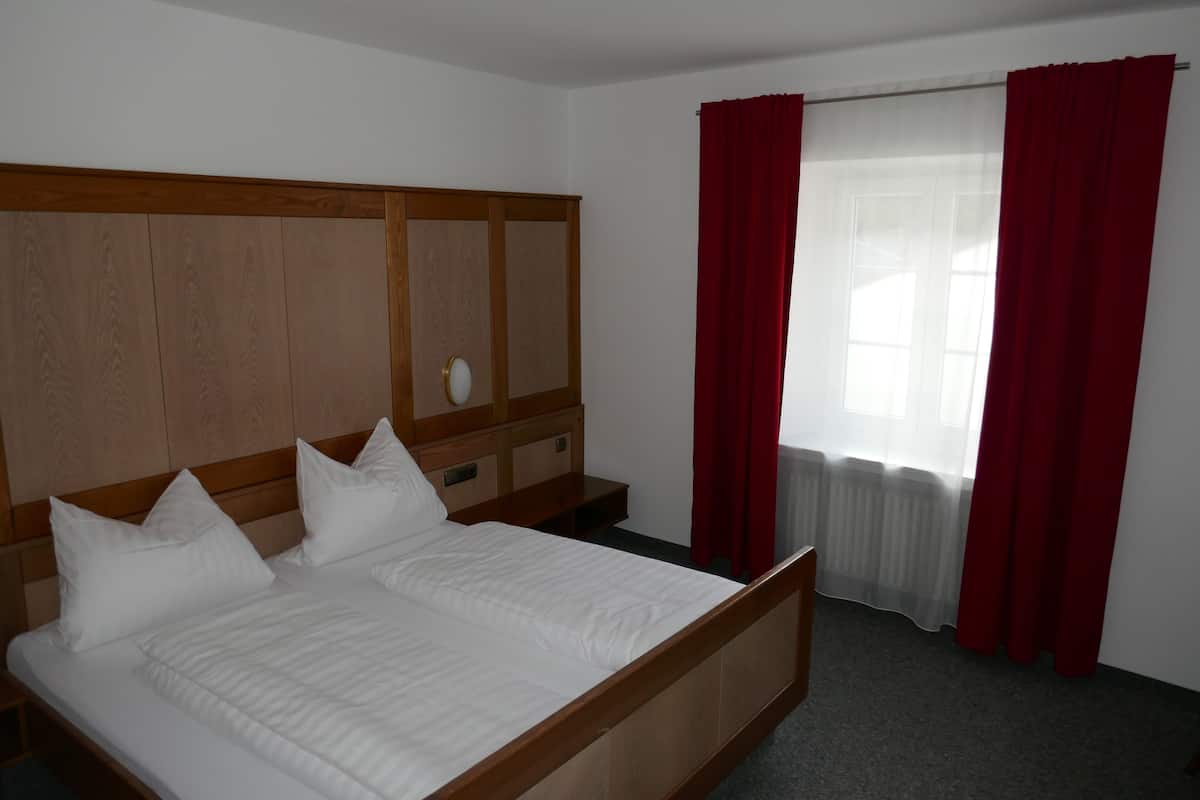 Een net opgemaakt bed met witte beddengoed, een houten hoofdbord en een nachtkastje met een lamp.