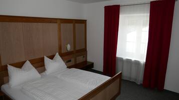 A neatly made bed with white bedding, a wooden headboard, and a nightstand with a lamp.